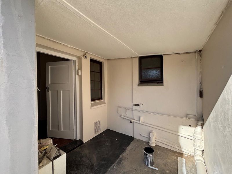 A functional utility or service area featuring exposed plumbing, a timber door, and basic finishes, suitable for conversion or storage improvement.