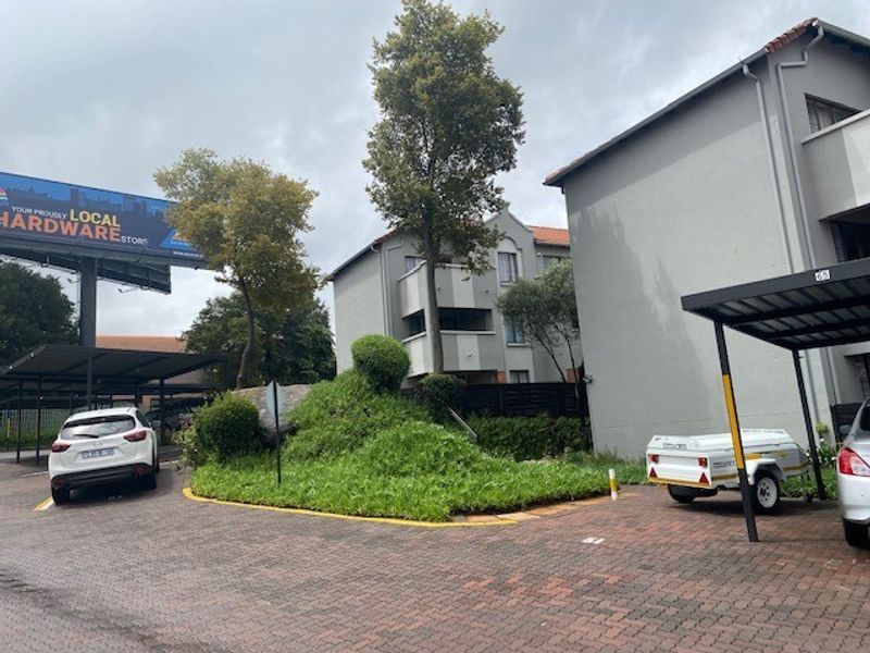 Exterior view of the apartment complex featuring paved driveway, covered parking bays, and established garden landscaping.