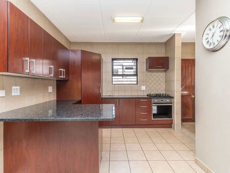 A functional kitchen featuring dark wood cabinetry, granite countertops, a built-in oven with gas hob, and neutral tiled flooring and backsplash.