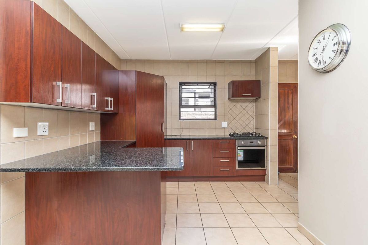 A functional kitchen featuring dark wood cabinetry, granite countertops, a built-in oven with gas hob, and neutral tiled flooring and backsplash.
