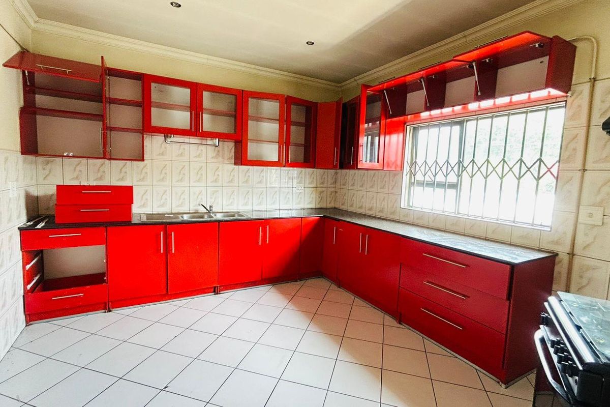 A kitchen featuring red cabinetry, tiled splashbacks, tiled flooring, and a window with security bars.