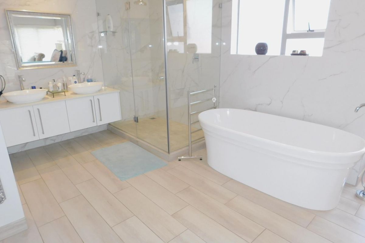 Modern bathroom featuring a double vanity, glass-enclosed walk-in shower, and a freestanding bathtub with marble-look wall tiling and light wood-look floor tiles.