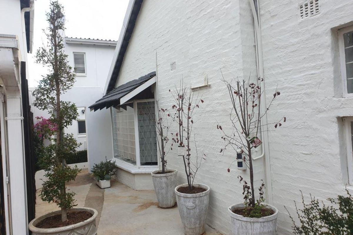 A side courtyard area featuring painted brick walls, concrete paving, and a bay window with a tiled awning.