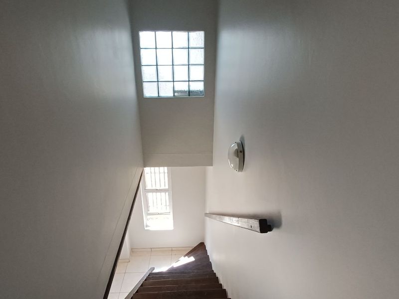 A functional staircase hallway featuring a glass block window for natural light, a wall-mounted handrail, and a simple light fixture.