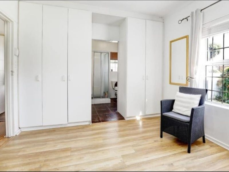 A bedroom featuring light-toned laminate flooring, extensive built-in cupboards, and direct access to an en-suite bathroom.