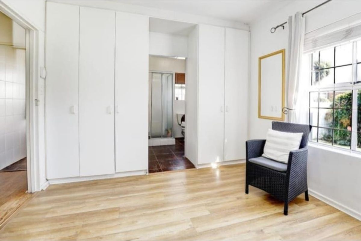 A bedroom featuring light-toned laminate flooring, extensive built-in cupboards, and direct access to an en-suite bathroom.