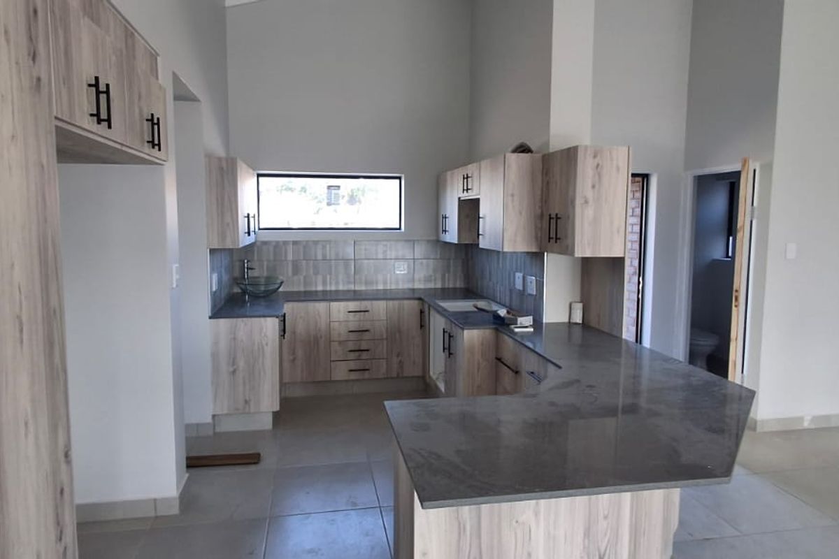 Modern kitchen featuring light wood-grain cabinetry, dark stone countertops, a breakfast bar, and a tiled backsplash in an open-plan layout.