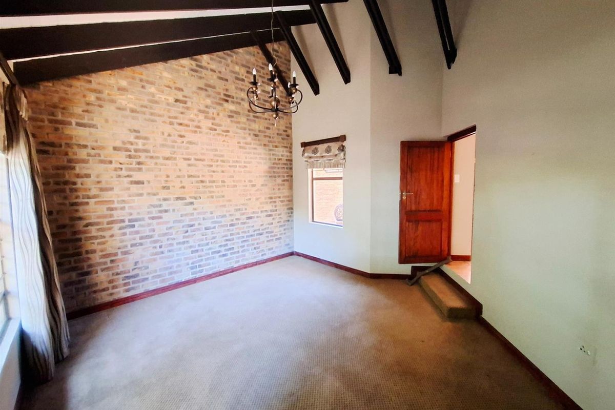 Spacious bedroom featuring a vaulted ceiling with exposed timber beams, a rustic exposed brick feature wall, and carpeted flooring.