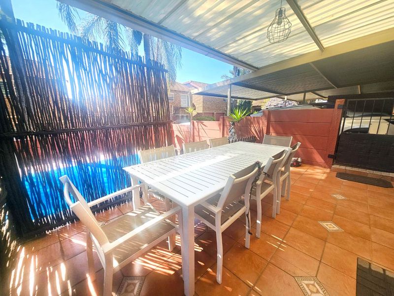 A covered outdoor patio area featuring tiled flooring, a metal roof structure, and a privacy screen, providing a functional space for outdoor dining.