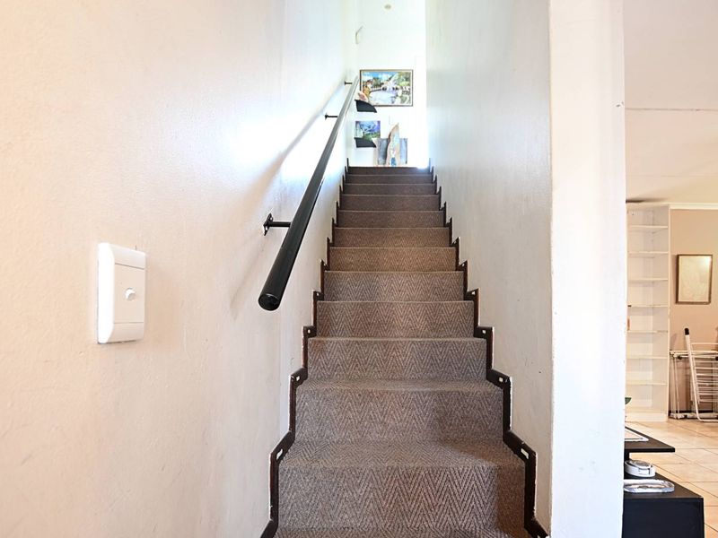 A carpeted staircase featuring a black handrail, leading to an upper level with visible wear on the wall finishes and stair carpeting.