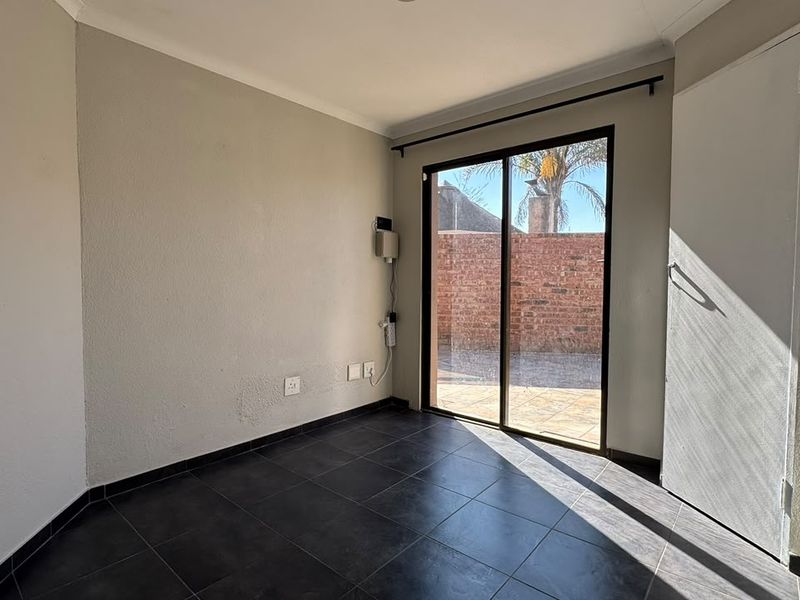 An empty bedroom featuring dark tiled flooring, a built-in cupboard, and a sliding glass door providing access to the rear exterior area.
