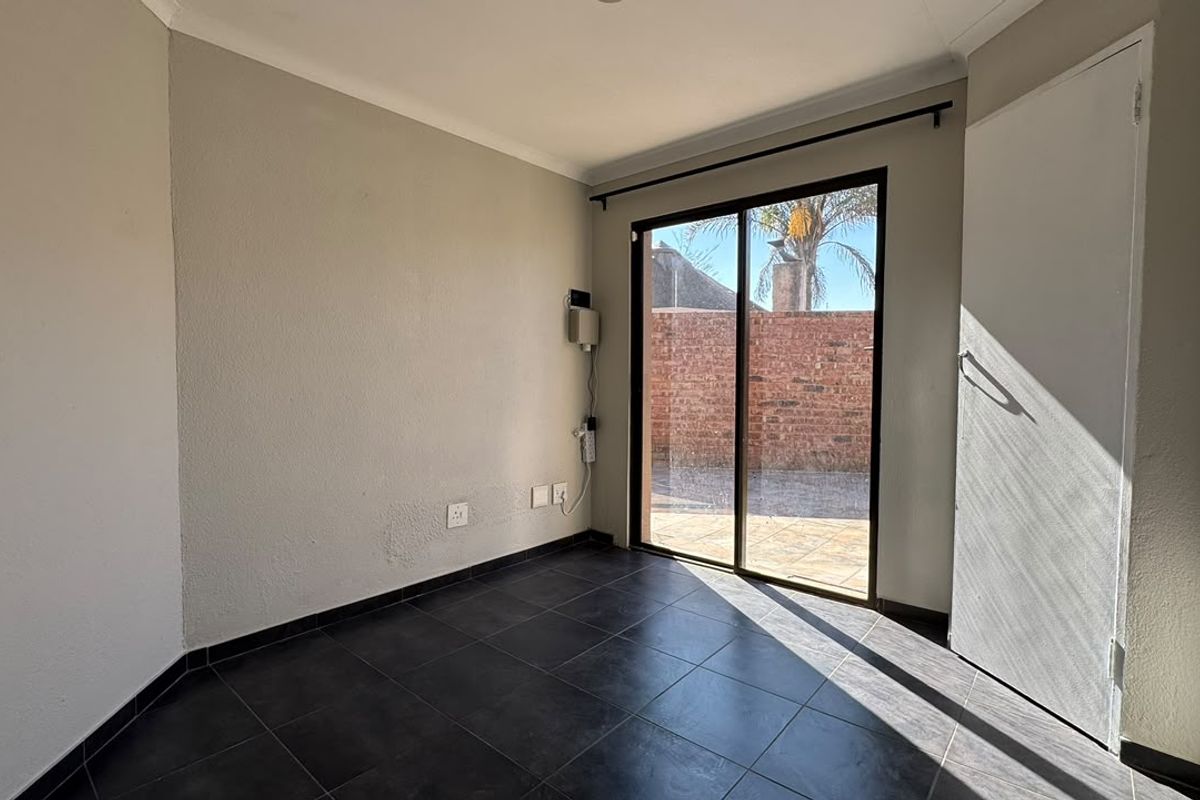 An empty bedroom featuring dark tiled flooring, a built-in cupboard, and a sliding glass door providing access to the rear exterior area.