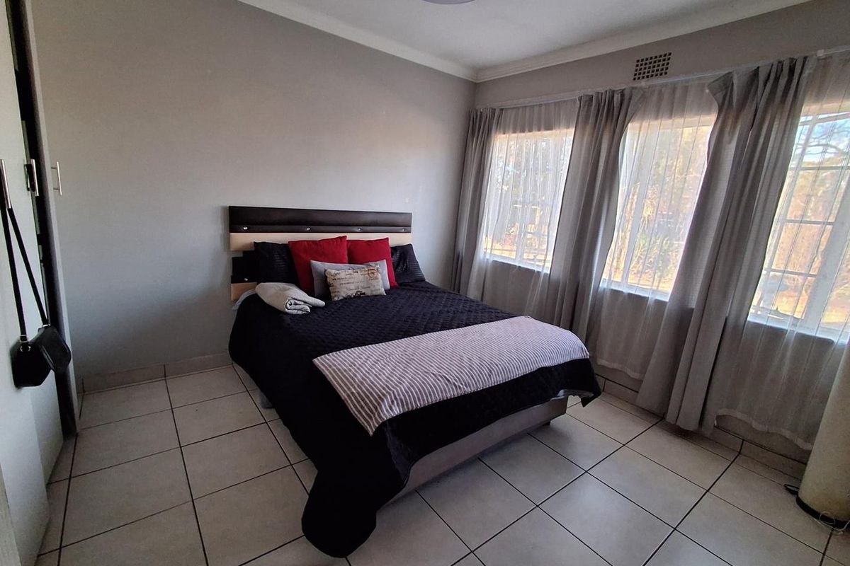A functional bedroom featuring tiled flooring, a built-in cupboard, and large windows that provide natural light.