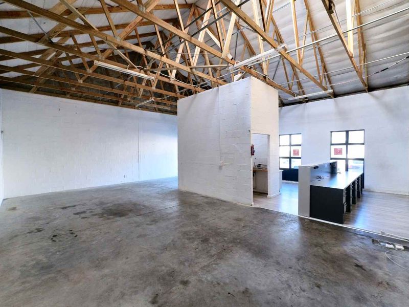 Spacious industrial unit featuring exposed timber roof trusses, concrete flooring, and a central partitioned area with a built-in reception counter.
