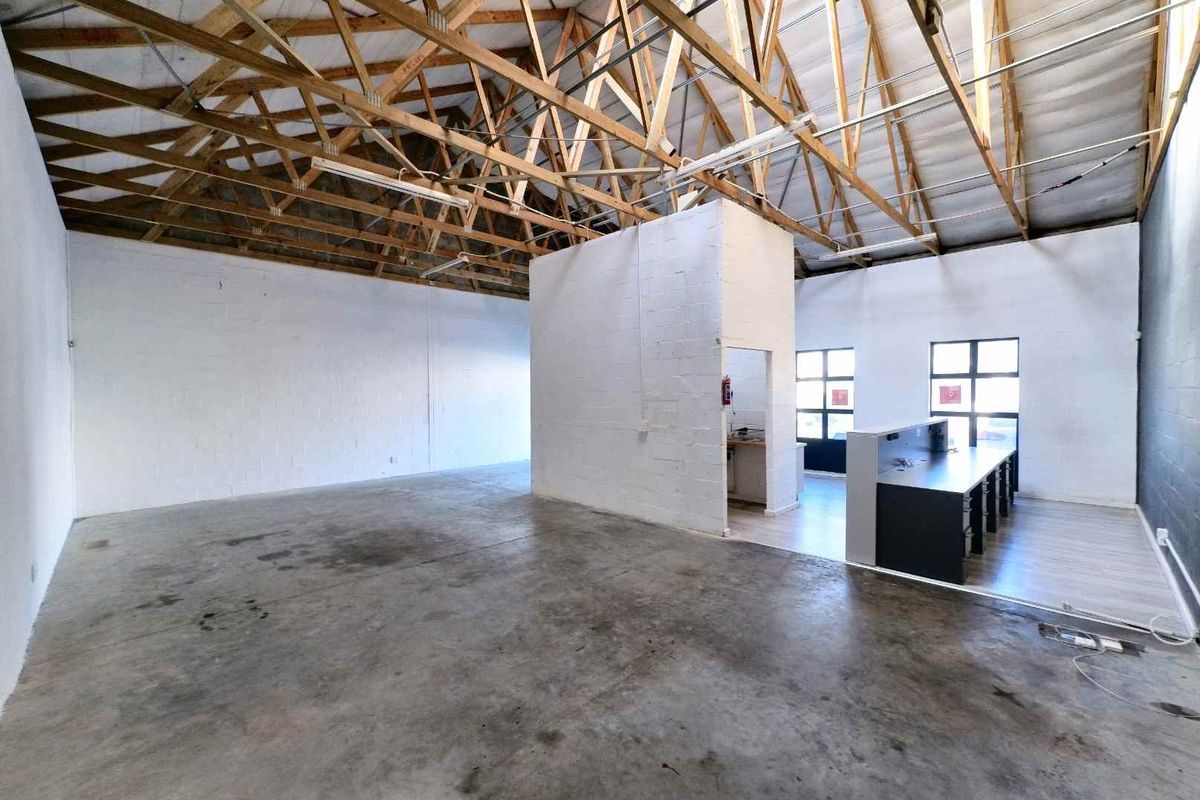 Spacious industrial unit featuring exposed timber roof trusses, concrete flooring, and a central partitioned area with a built-in reception counter.