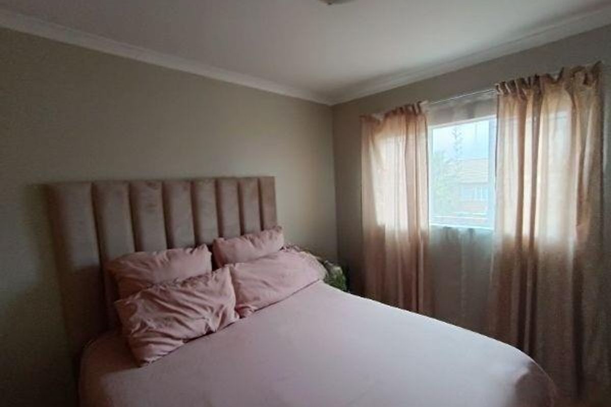 A cozy bedroom featuring neutral wall tones, a flush mount ceiling light, and a window with curtains, providing a comfortable and functional sleeping space.