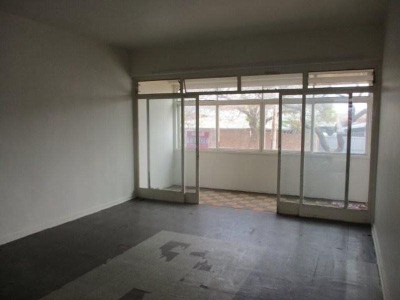 An empty living room featuring large sliding glass doors leading to a balcony, with worn flooring in need of replacement.