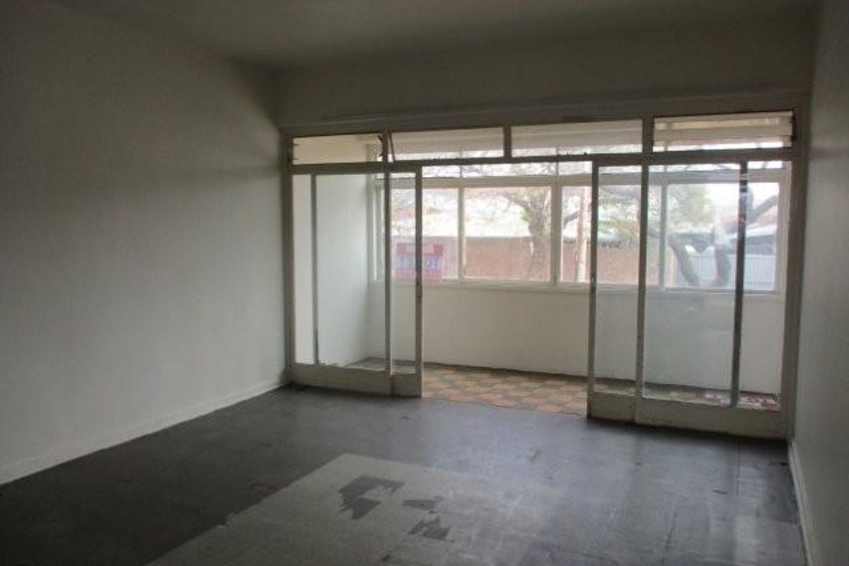 An empty living room featuring large sliding glass doors leading to a balcony, with worn flooring in need of replacement.