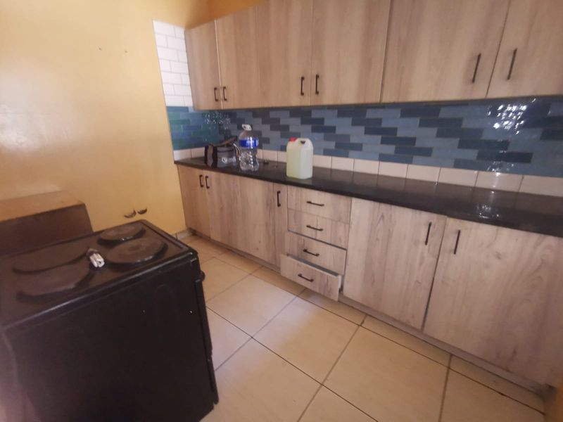 A functional kitchen featuring light wood-look cabinetry, dark countertops, a tiled backsplash, and tiled flooring, providing a practical workspace for daily cooking.