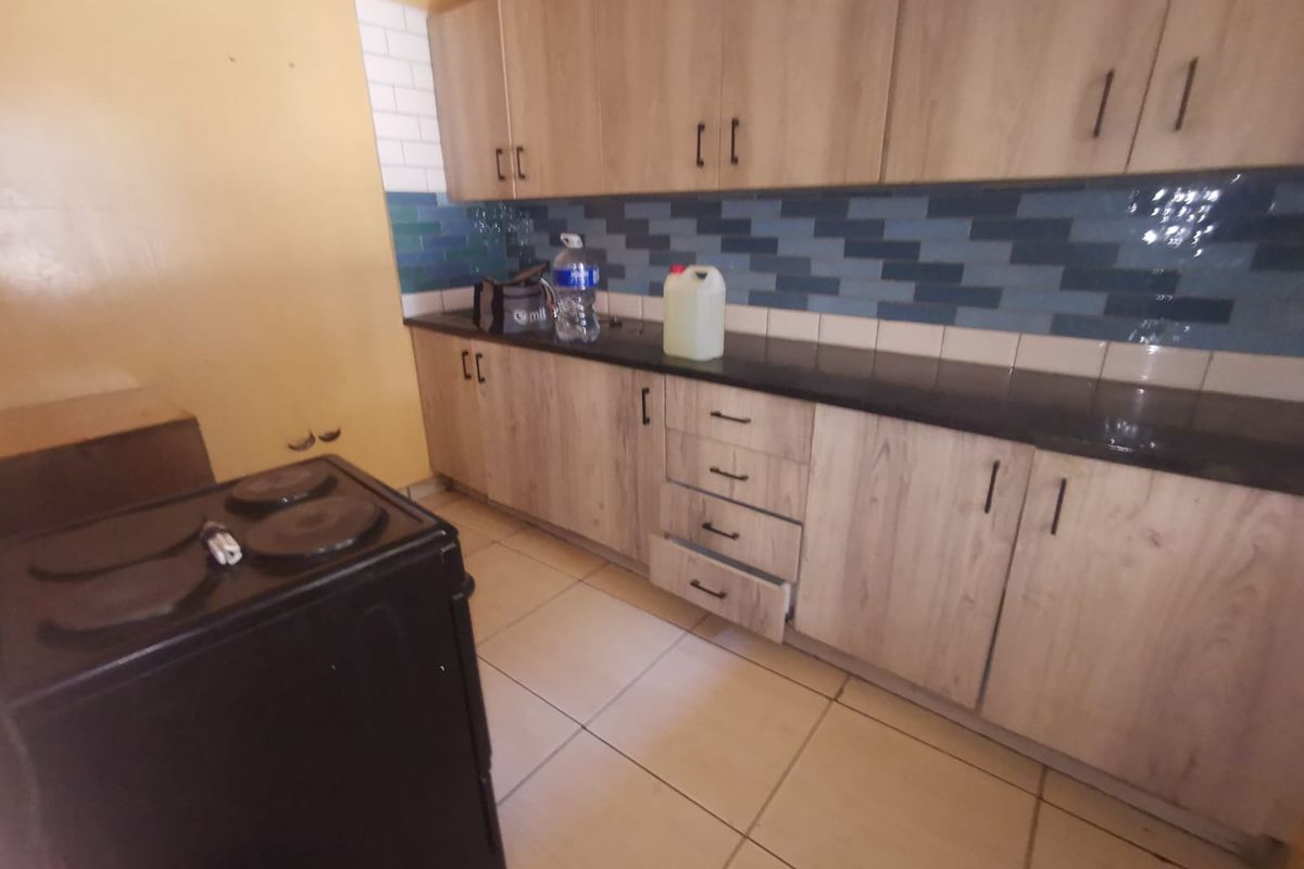 A functional kitchen featuring light wood-look cabinetry, dark countertops, a tiled backsplash, and tiled flooring, providing a practical workspace for daily cooking.