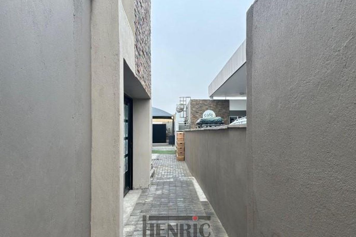 A paved side walkway or exterior passage connecting different sections of the mixed-use property, featuring rendered boundary walls and stone cladding accents.