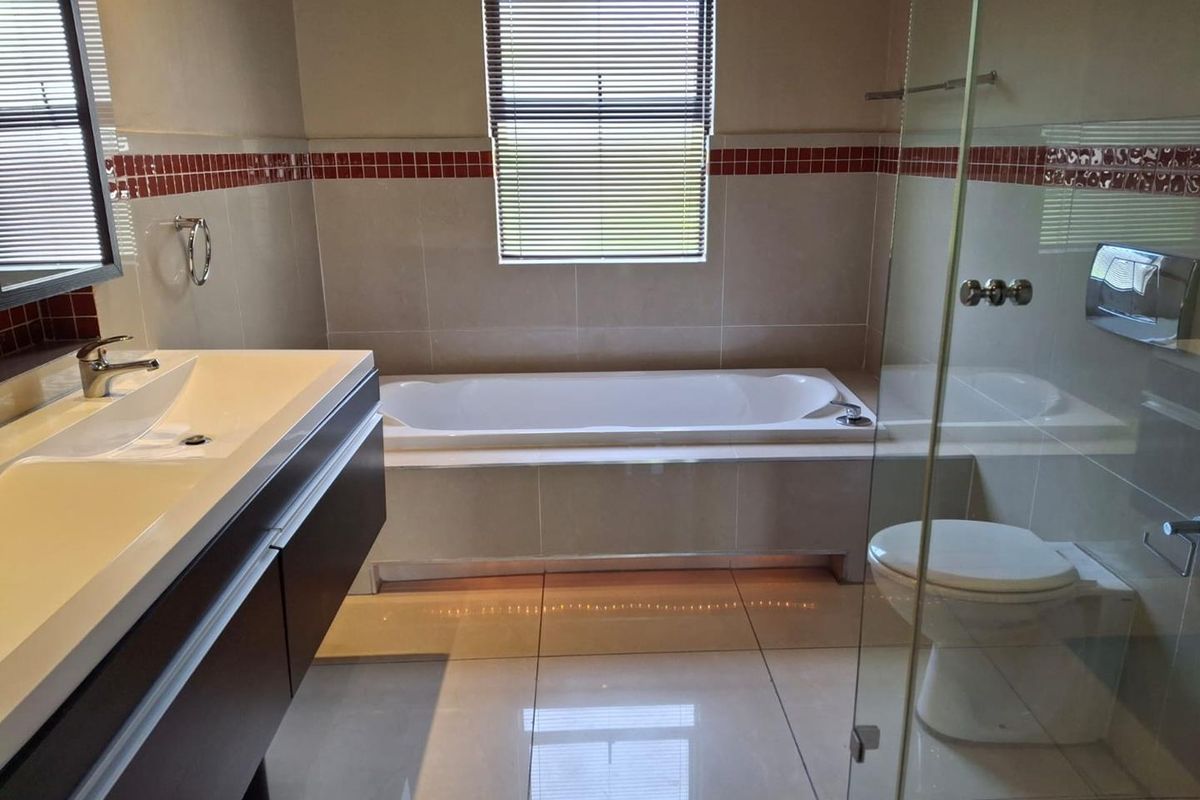Modern bathroom featuring a built-in vanity, bathtub, glass-enclosed shower, and wall-mounted toilet with neutral tiling and decorative accent borders.