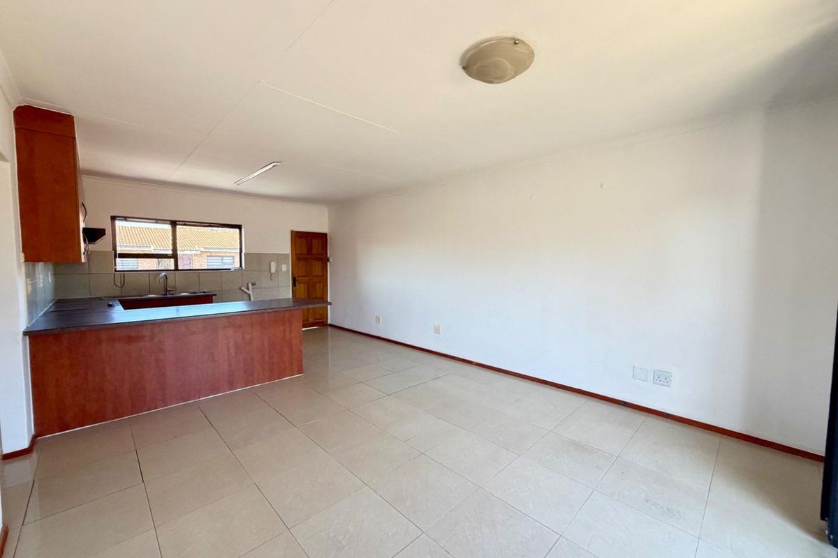An open-plan living and kitchen area featuring tiled flooring, wooden cabinetry, and a breakfast counter, providing a versatile and bright living space.
