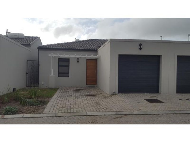 Front elevation of a modern residential property featuring a paved driveway, single garage, timber entrance door, and a small pergola.
