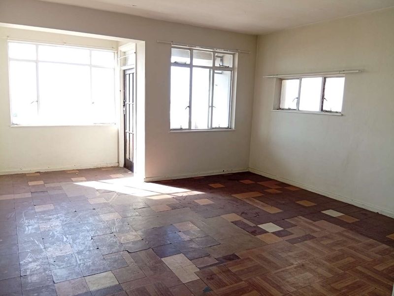 An empty living room featuring original parquet flooring and large windows, offering a blank canvas for renovation and interior design updates.
