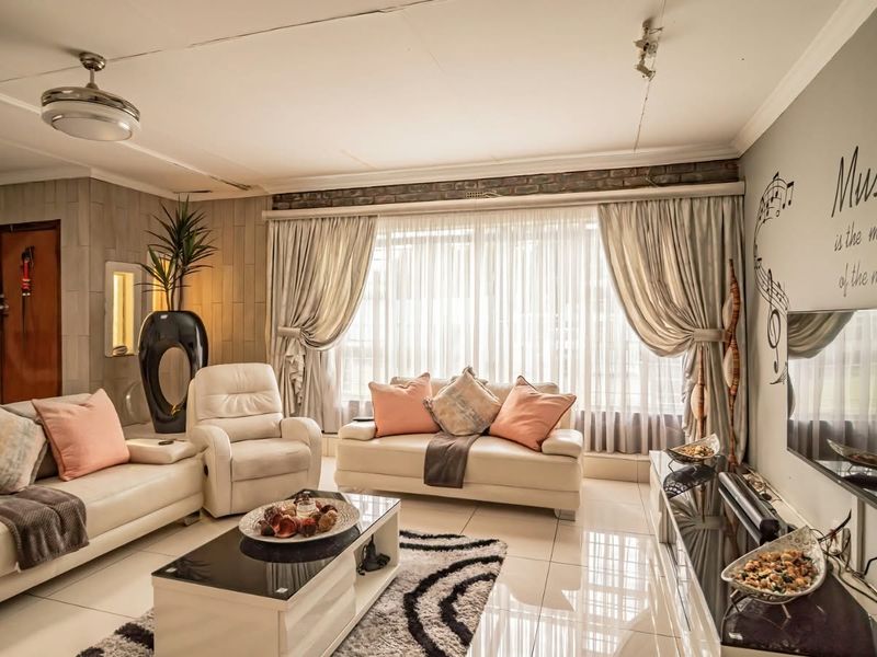 A spacious living room featuring tiled flooring, exposed brick accents, and a ceiling fan, offering a comfortable area for relaxation.