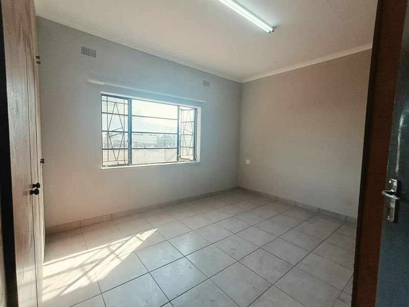 A vacant bedroom featuring tiled flooring, built-in cupboards, and a steel-framed window with security bars, offering a neutral canvas for potential updates.