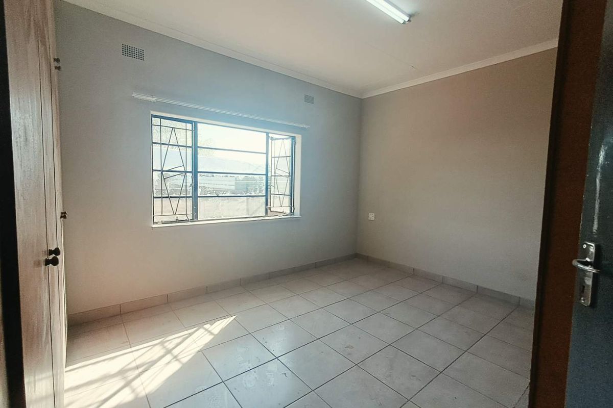 A vacant bedroom featuring tiled flooring, built-in cupboards, and a steel-framed window with security bars, offering a neutral canvas for potential updates.