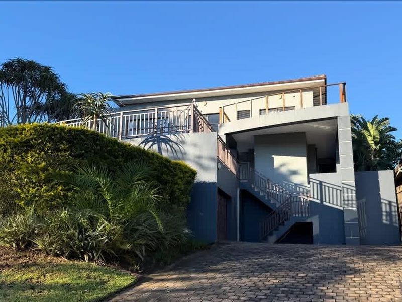 Front elevation of a multi-level house featuring a paved driveway, elevated deck, and external staircase leading to the upper level.