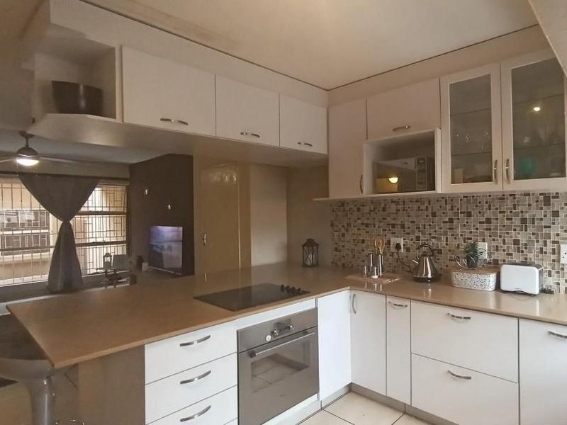 A functional kitchen featuring built-in cabinetry, a mosaic tile backsplash, integrated electric hob and oven, and a convenient breakfast bar counter.