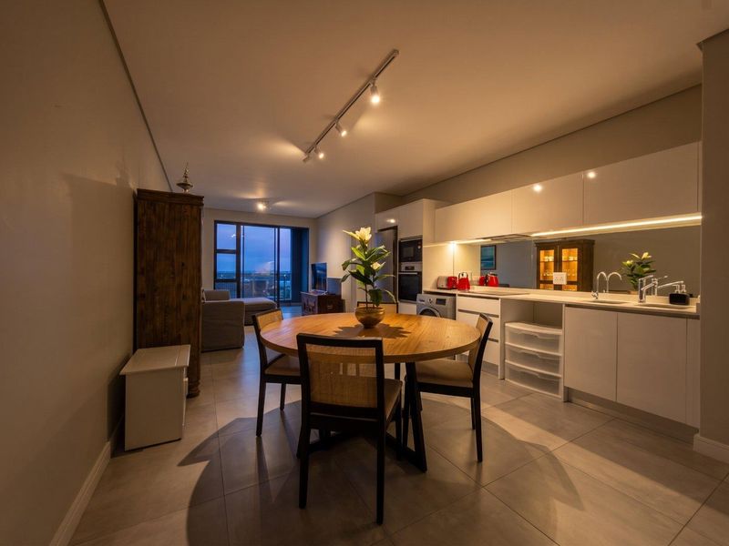 Modern open-plan living and kitchen area featuring sleek cabinetry, integrated appliances, tiled flooring, and track lighting, leading to a balcony with views.