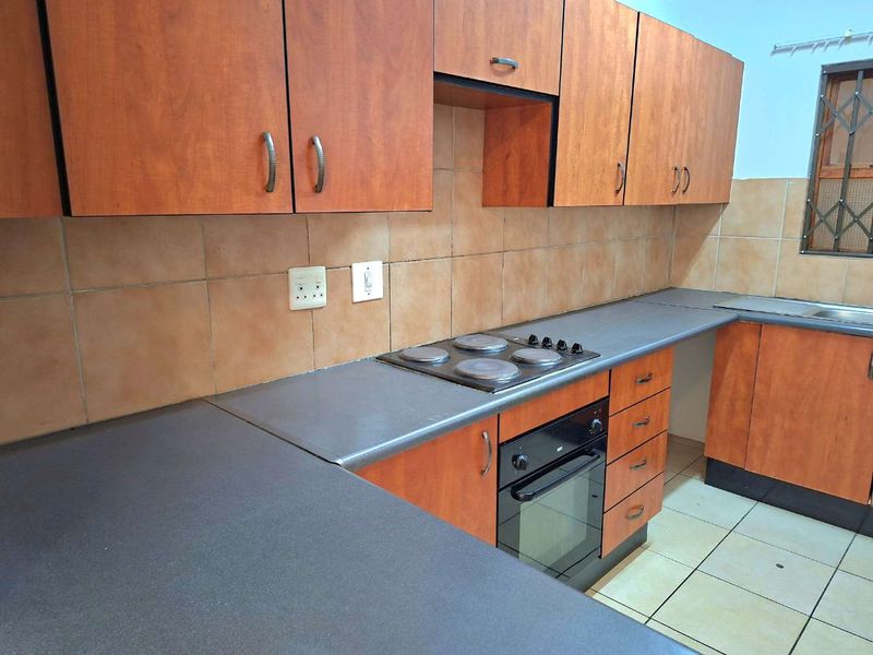 A functional kitchen featuring wood-look laminate cabinetry, built-in oven and hob, tiled backsplash, and ample countertop workspace.