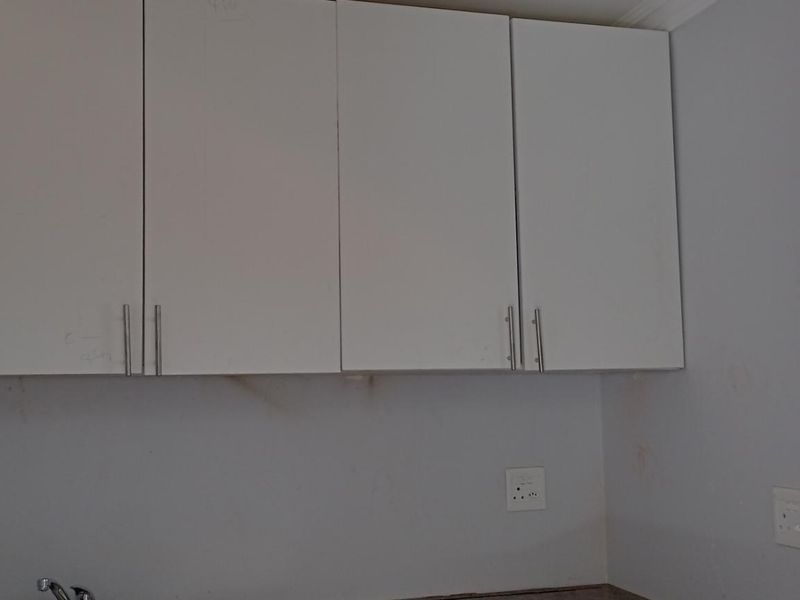 A compact scullery or utility area featuring wall-mounted white cabinetry, a sink faucet, and electrical points, requiring minor cosmetic updates.