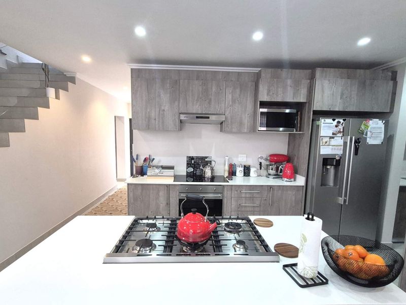 Modern kitchen featuring a central island with a gas hob, sleek laminate cabinetry, built-in appliances, and an adjacent staircase.
