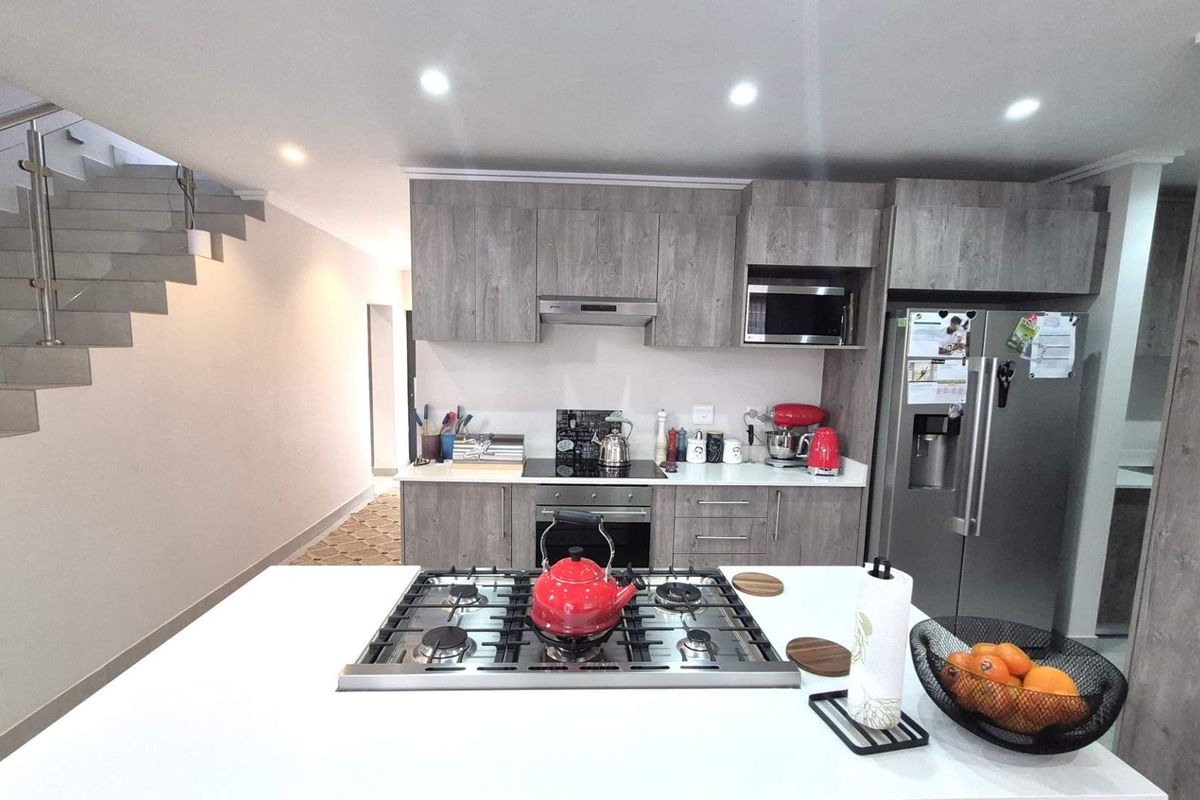 Modern kitchen featuring a central island with a gas hob, sleek laminate cabinetry, built-in appliances, and an adjacent staircase.