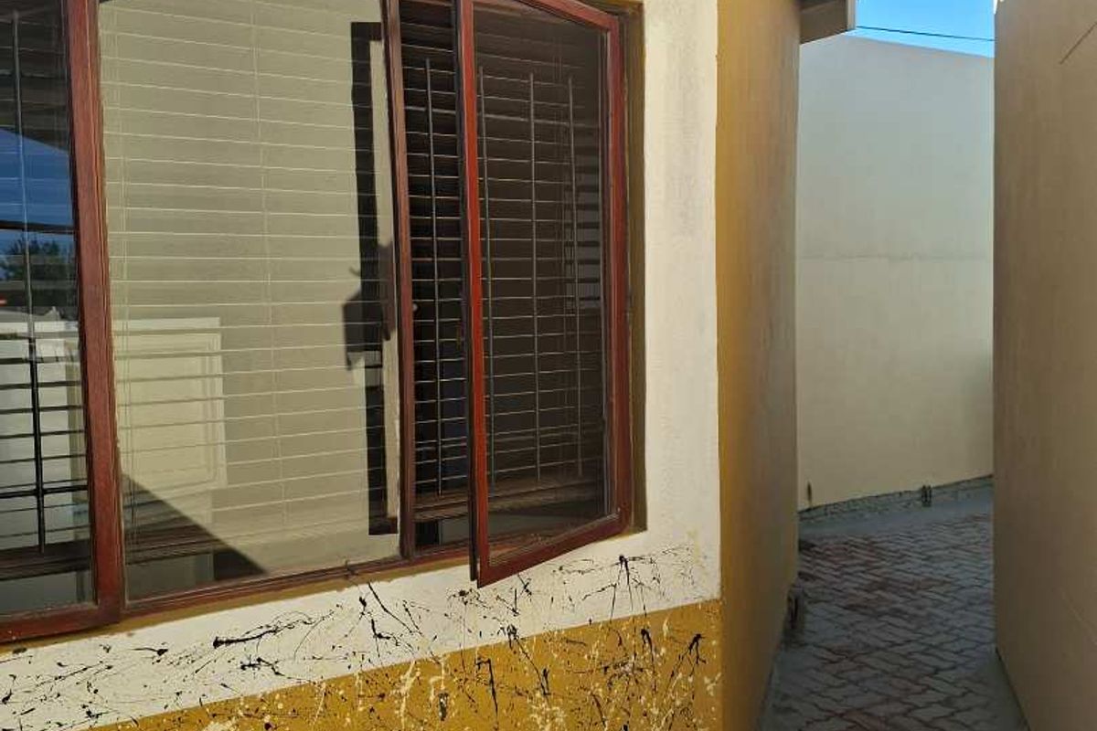 A narrow side passage featuring paved flooring and an exterior wall with visible paint damage and an aluminium window with a security screen.
