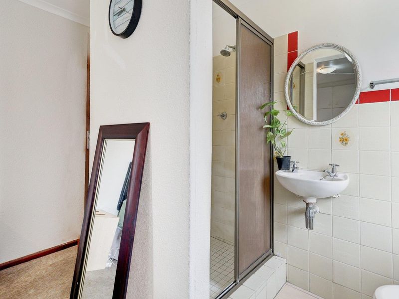 A compact bathroom featuring a shower enclosure and a wall-mounted basin with tiled walls, presenting an opportunity for modernization.
