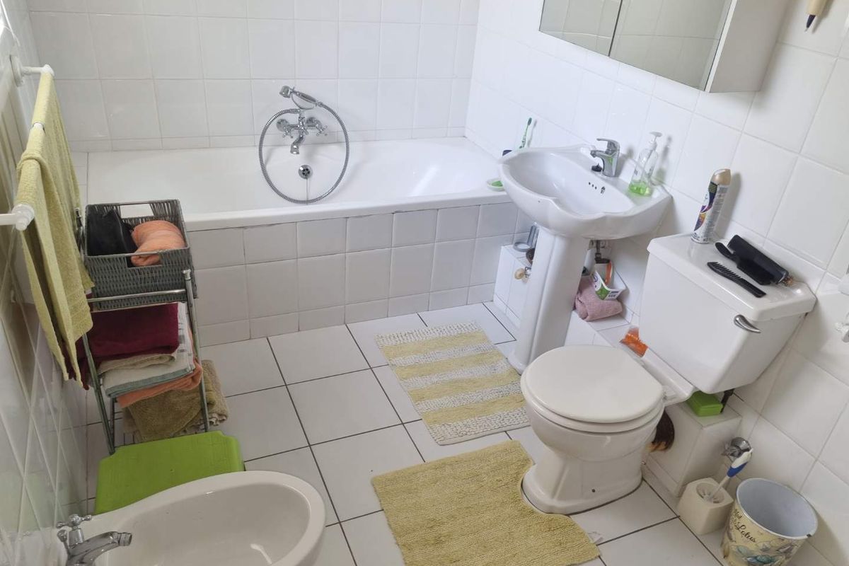 A functional bathroom featuring a white bathtub, pedestal basin, toilet, and bidet with full-height wall tiling and tiled flooring.