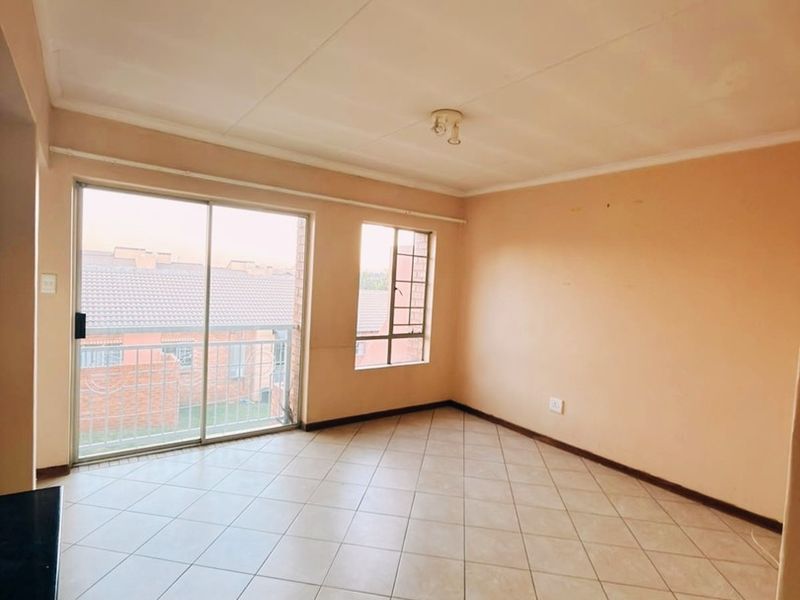 An empty, open-plan living area featuring neutral tiled flooring, large windows, and a sliding door providing access to a balcony.