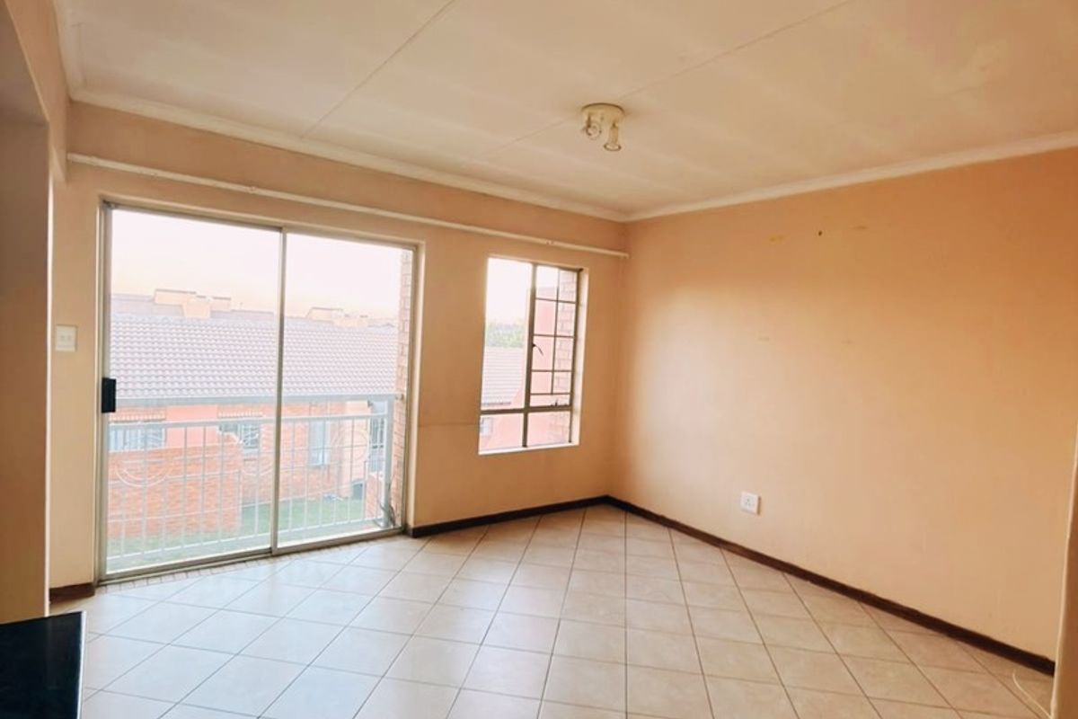 An empty, open-plan living area featuring neutral tiled flooring, large windows, and a sliding door providing access to a balcony.