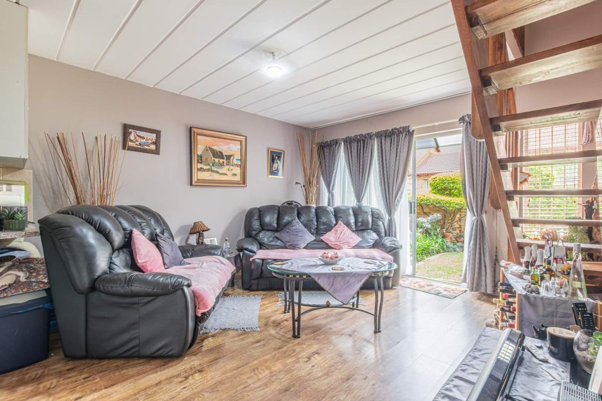 A living room featuring wood-look flooring, a timber staircase, and sliding glass doors providing direct access to the rear garden.