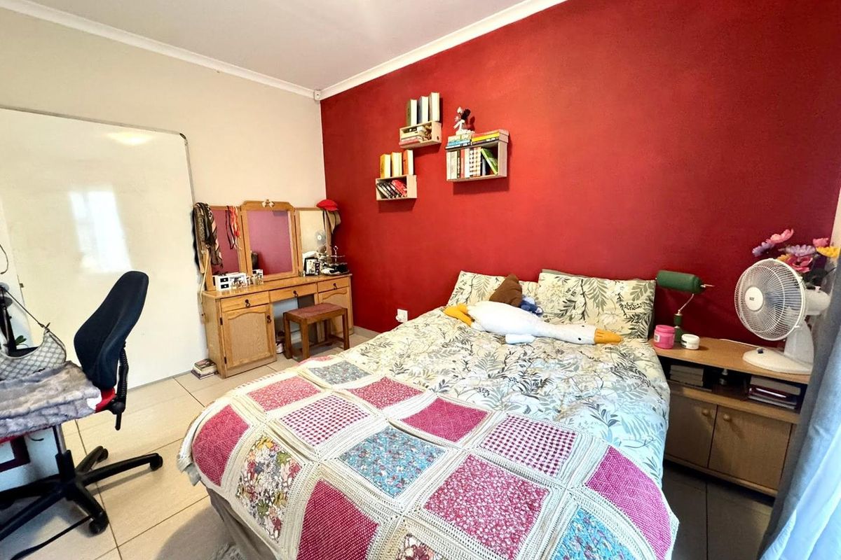A bedroom featuring tiled flooring and a bold red accent wall, providing a functional space with neutral wall finishes.