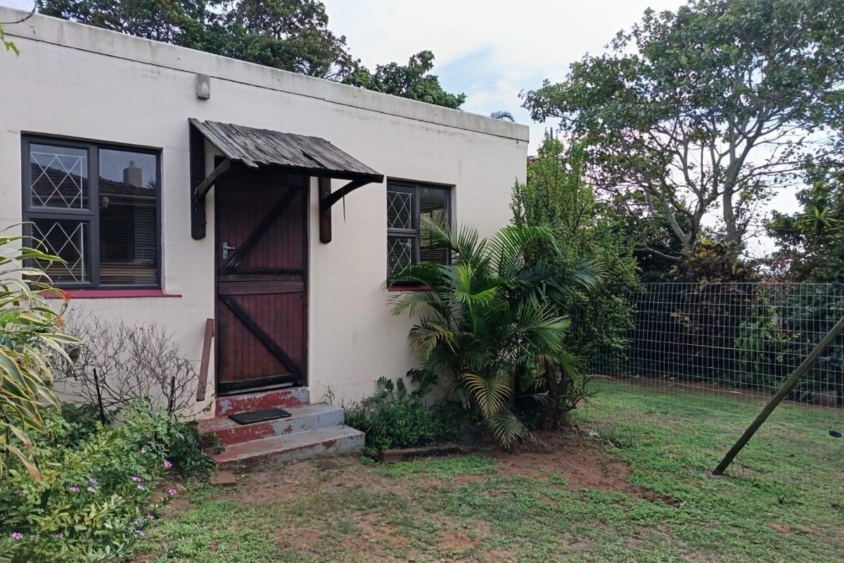 Rear exterior view of the property featuring a timber door with a small canopy, diamond-patterned windows, and concrete steps leading to the garden area.