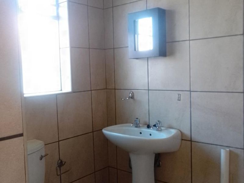 A functional bathroom featuring a pedestal basin, toilet, and full-height wall tiling, providing a clean and practical space.