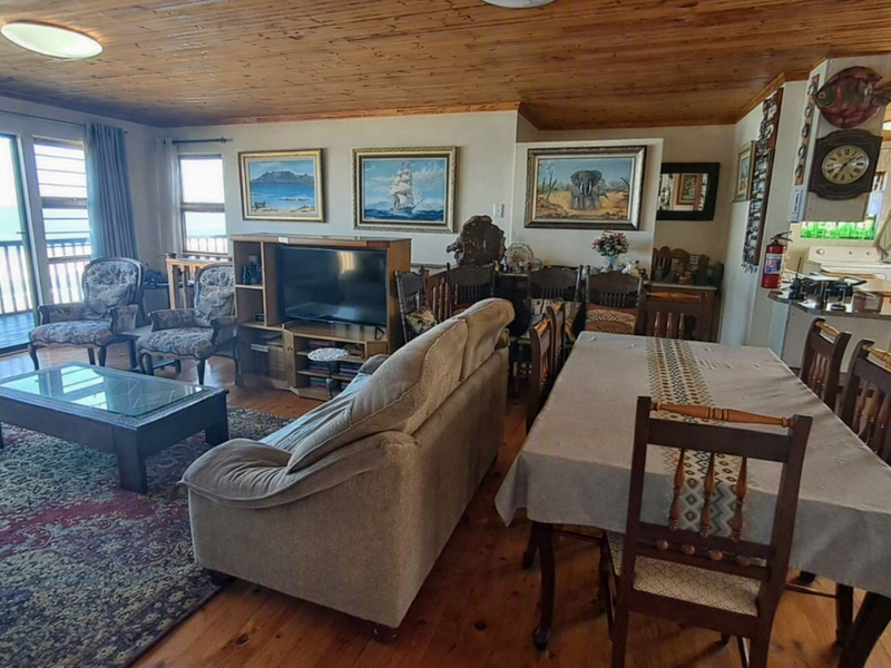 Spacious open-plan living and dining area featuring timber ceilings and flooring, with direct access to a balcony and an adjoining kitchen.