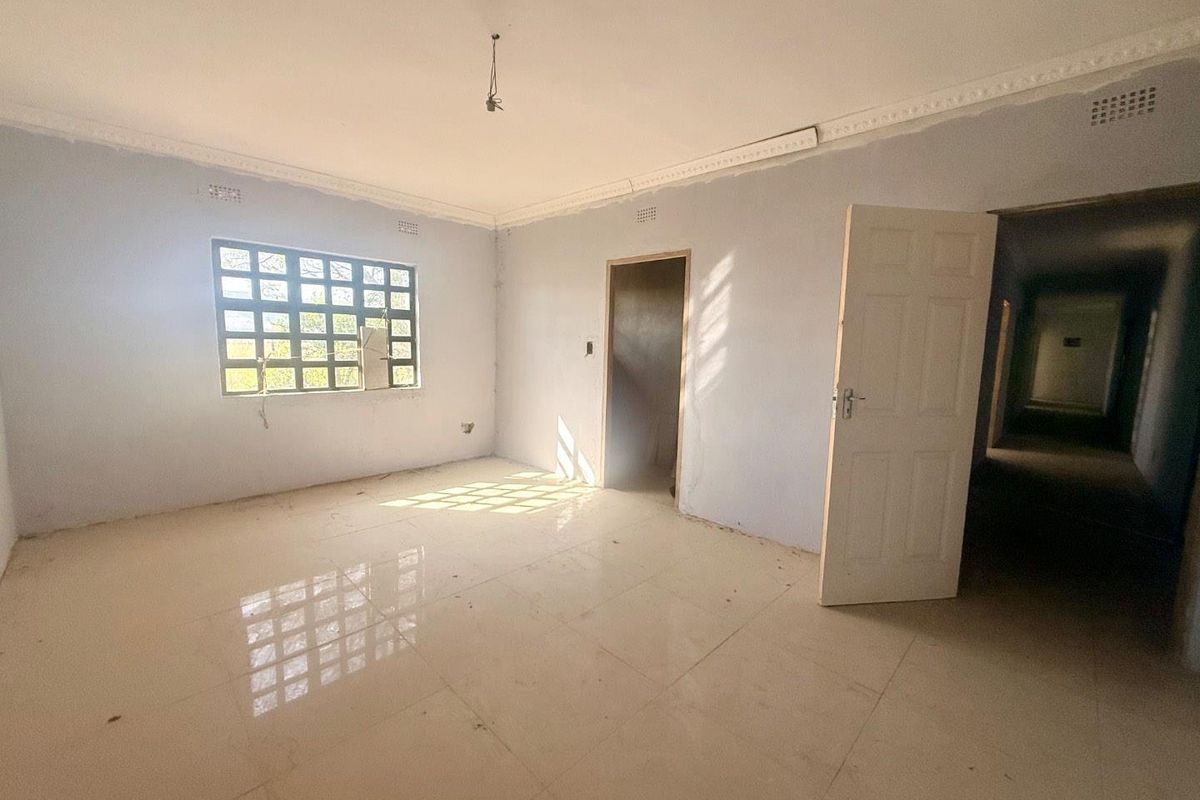 An empty, unfinished bedroom featuring tiled flooring, decorative ceiling cornices, and a window with a broken pane.